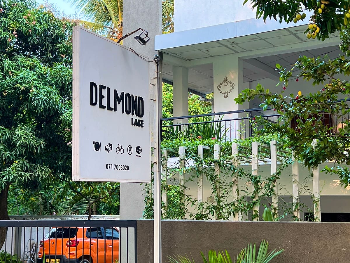 The DELMOND Lake sign at the entrance, with the guest house veranda and trees behind