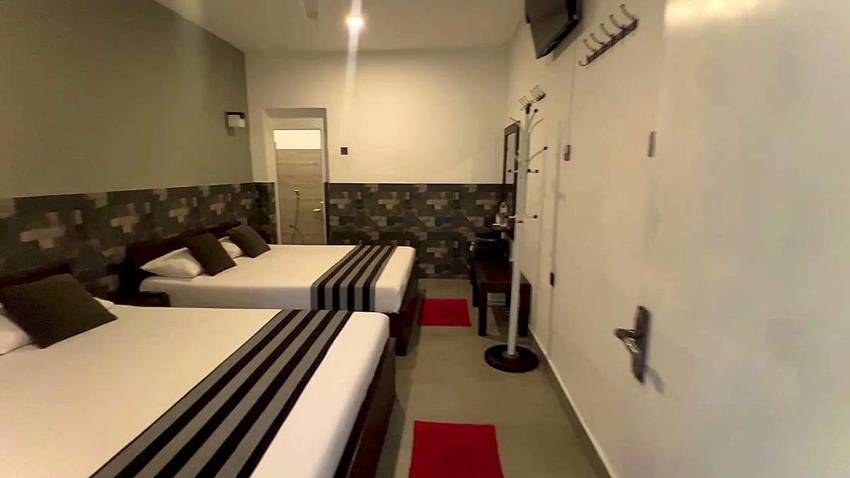 Family room with two beds dressed in white linen and grey runners, a wall-mounted fan and a doorway to the bathroom
